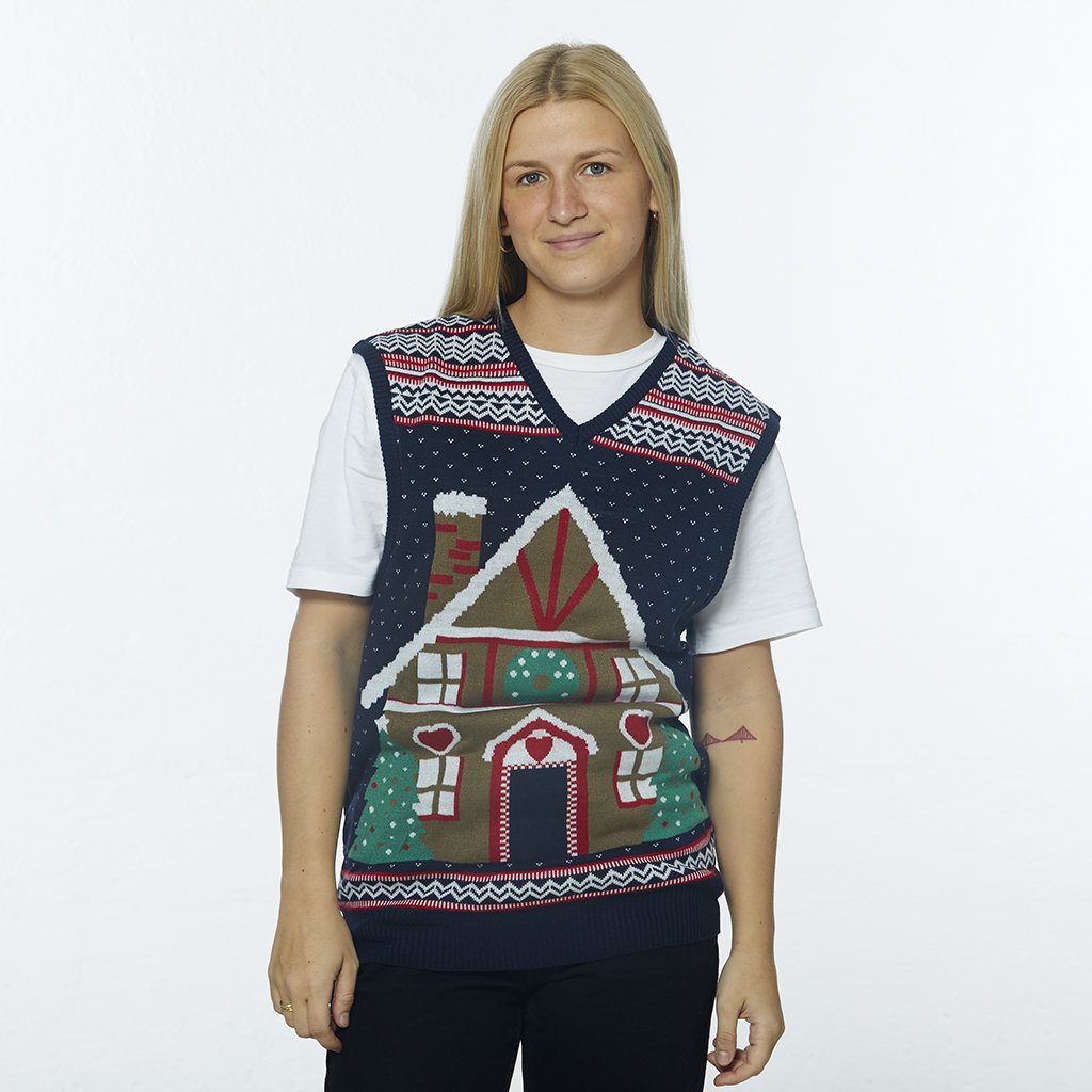 Une femme portant un gilet de Noël orné d'une maison en forme de gâteau.