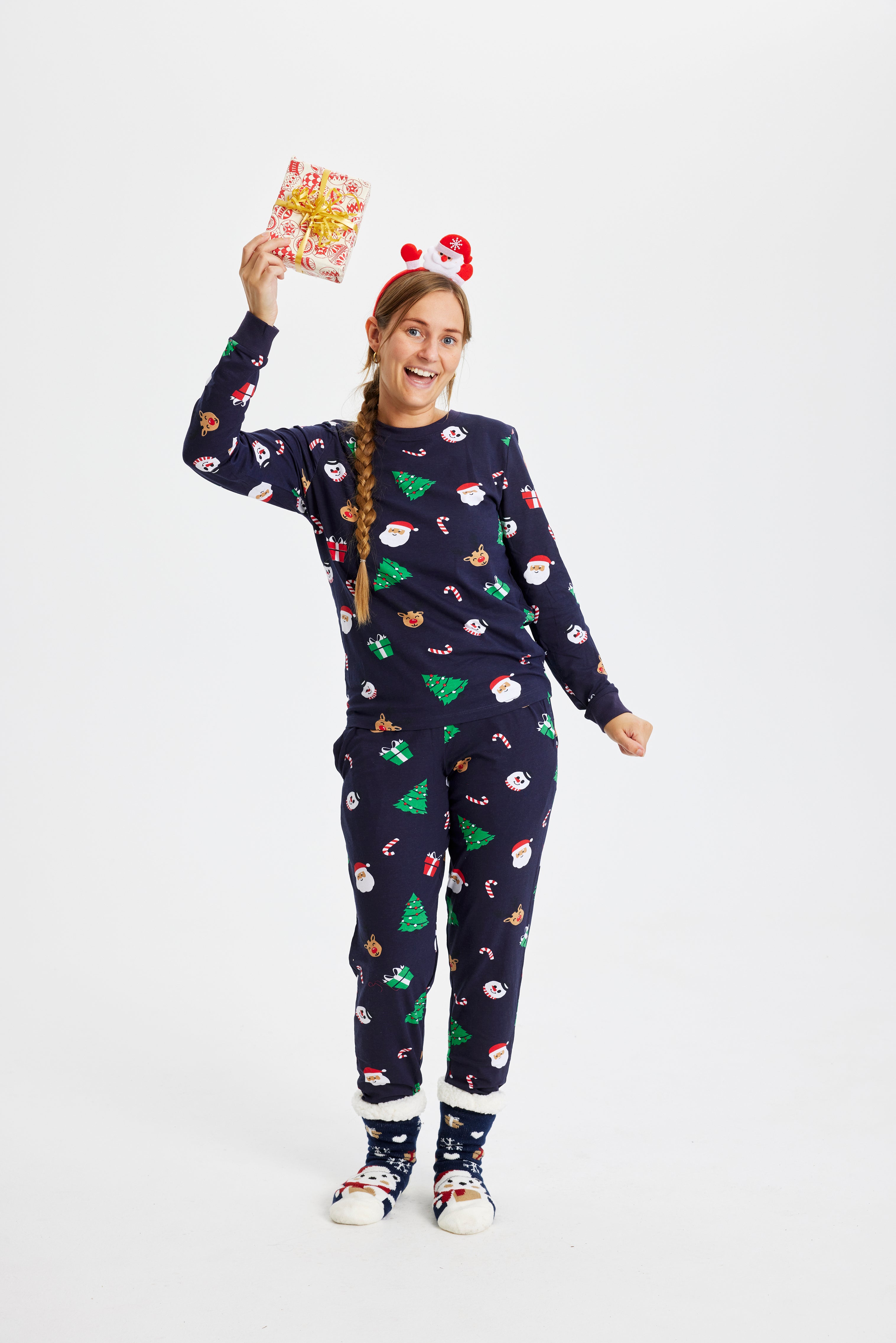 Une femme avec un cadeau portant un pyjama de Noël avec des arbres de Noël.