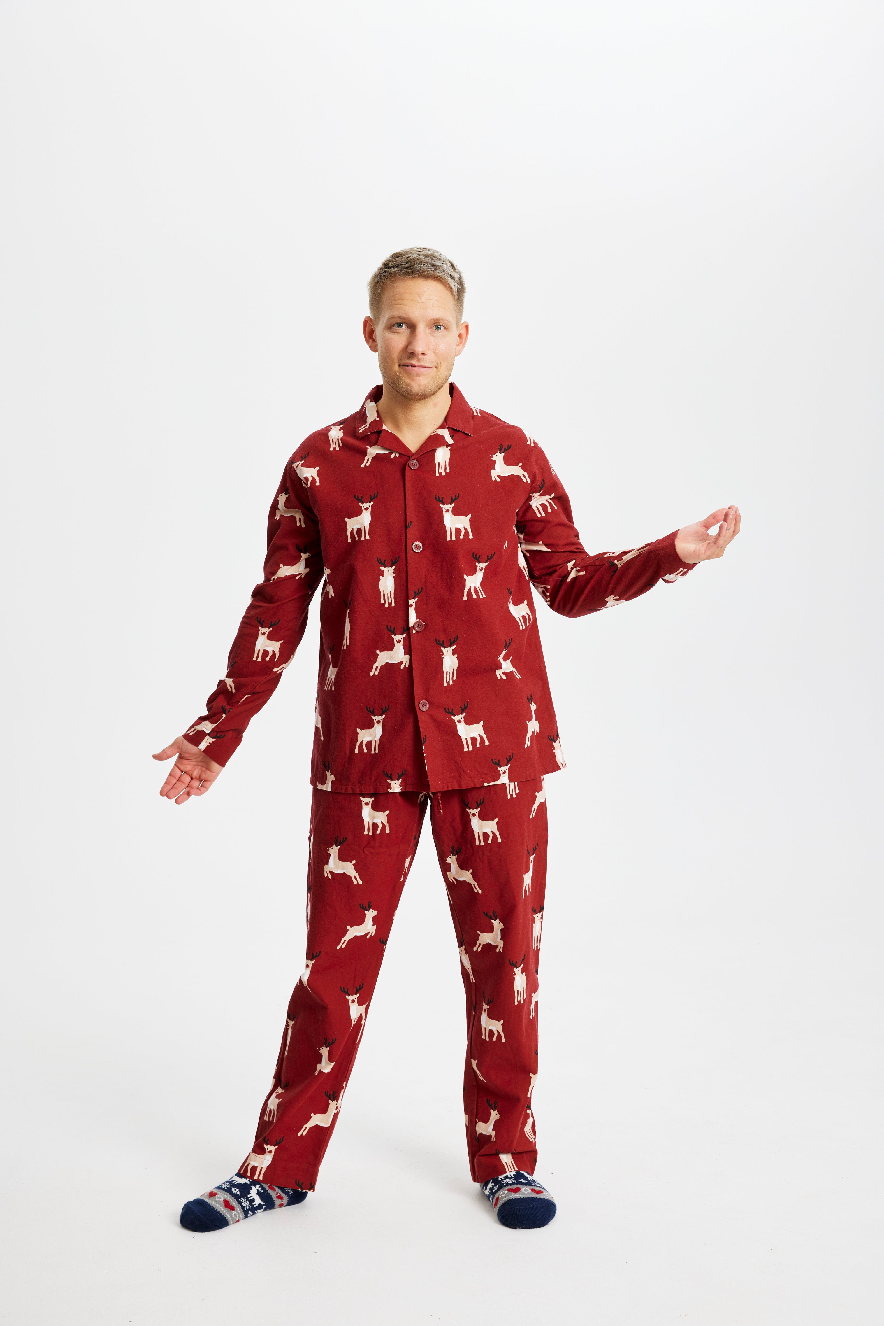 Un homme posant portant un pyjama de Noël rouge foncé avec des rennes.