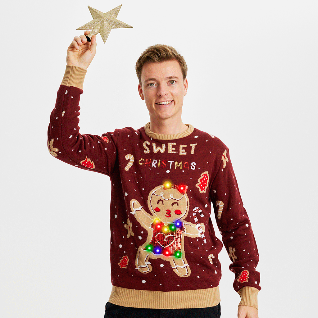 En mand iført en lysende julesweater står med en julestjerne i hånden hævet over hovedet.