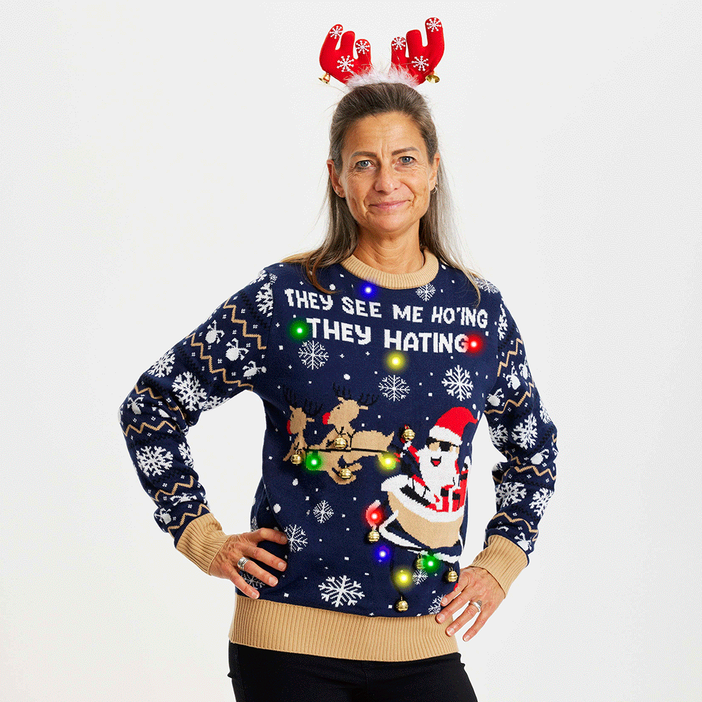 Une femme, les mains le long du corps, portant un pull de Noël jaune et bleu avec la citation 